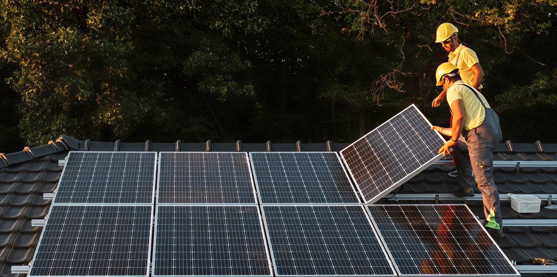 Zwei Installateure setzen im Abendlicht ein PV-Modul auf ein Ziegeldach